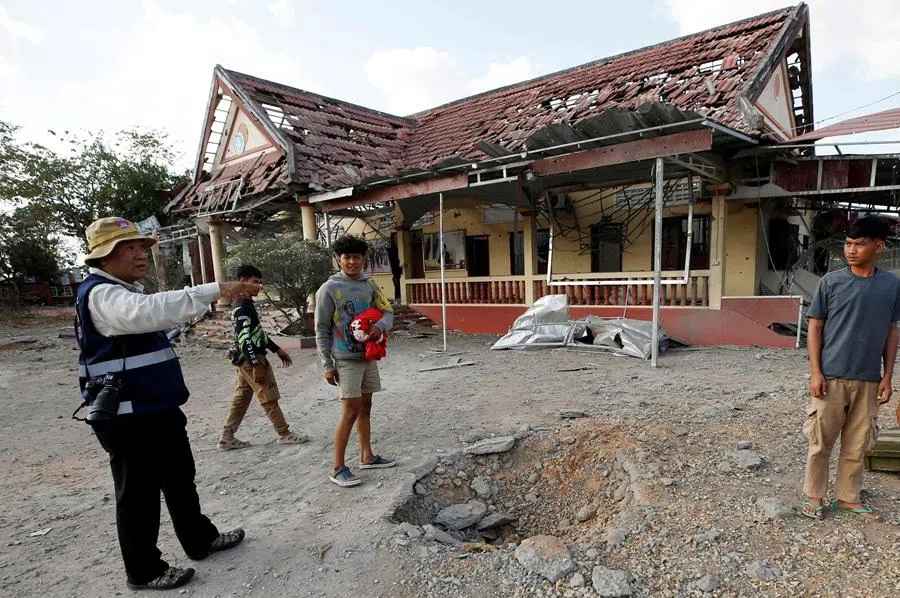 People stand beside a crater in front of a damaged police station following clashes between Cambodian and Thai soldiers in Boeung Trakoun village in Banteay Meanchey province on 3 January 2026. (AFP)