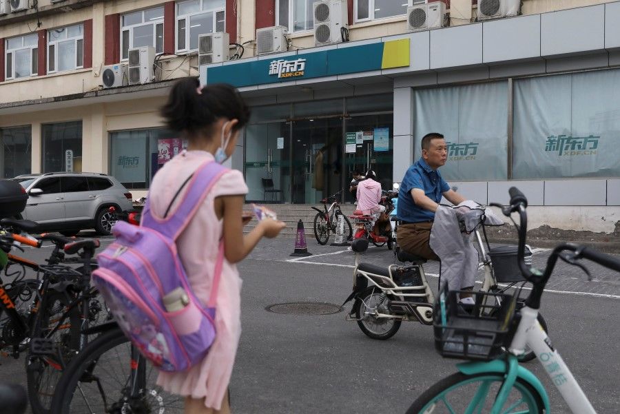 A girl carrying a schoolbag stands near an outlet of private educational services provider New Oriental Education and Technology Group in Beijing, China, 26 July 2021. REUTERS/Tingshu Wang