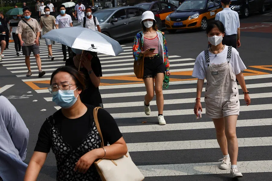 People wearing face masks walk across a street during morning rush hour, in Beijing, China, 2 August 2022. (Tingshu Wang/Reuters)