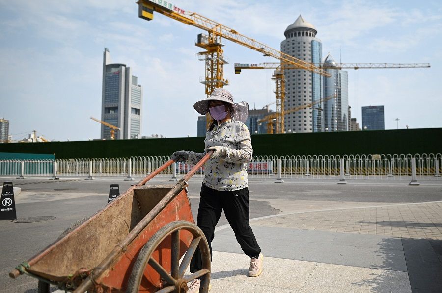 A worker pushes a trolley along a road outside a construction site at the central business district in Beijing, China, on 8 July 2022. (Wang Zhao/AFP)