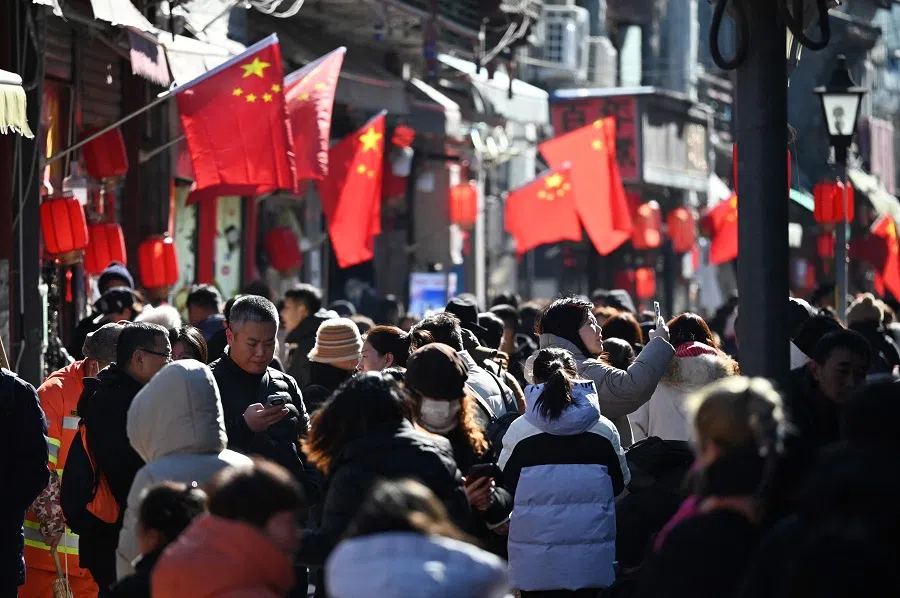People walk below Chinese flags in an alley near a popular shopping street in Beijing on 3 February 2025. (Greg Baker/AFP)