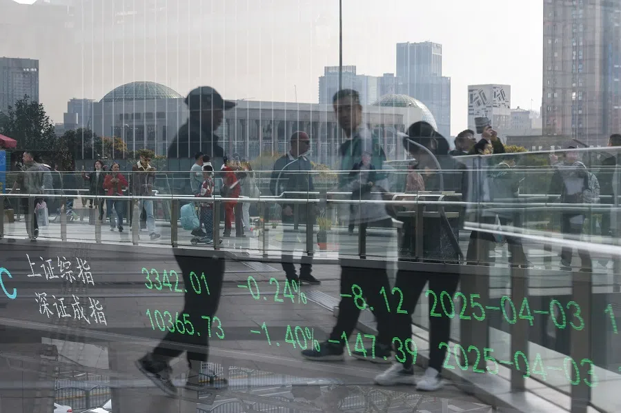 An electronic board shows Shanghai and Shenzhen stock indices as people walk on a pedestrian bridge at the Lujiazui financial district in Shanghai, China, on 3 April 2025.