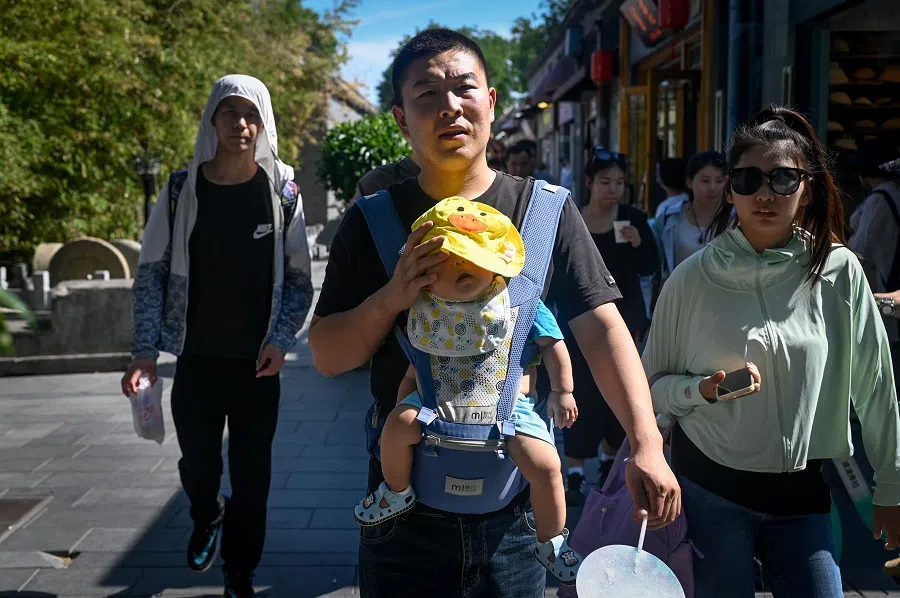 A man carrying a baby visits a business alley in Beijing, China, on 15 June 2024. (Wang Zhao/AFP)