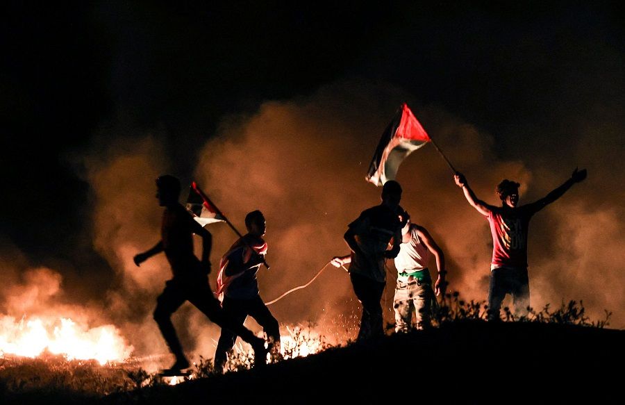 Palestinian protesters lift national flags as they burn tyres during a demonstration east of Gaza City by the border with Israel, on 15 June 2021, to protest the Israeli ultra-nationalist 'March of the Flags' in Jerusalem's Old City which celebrates the anniversary of Israel's 1967 occupation of Jerusalem's eastern sector. (Mahmud Hams/AFP)