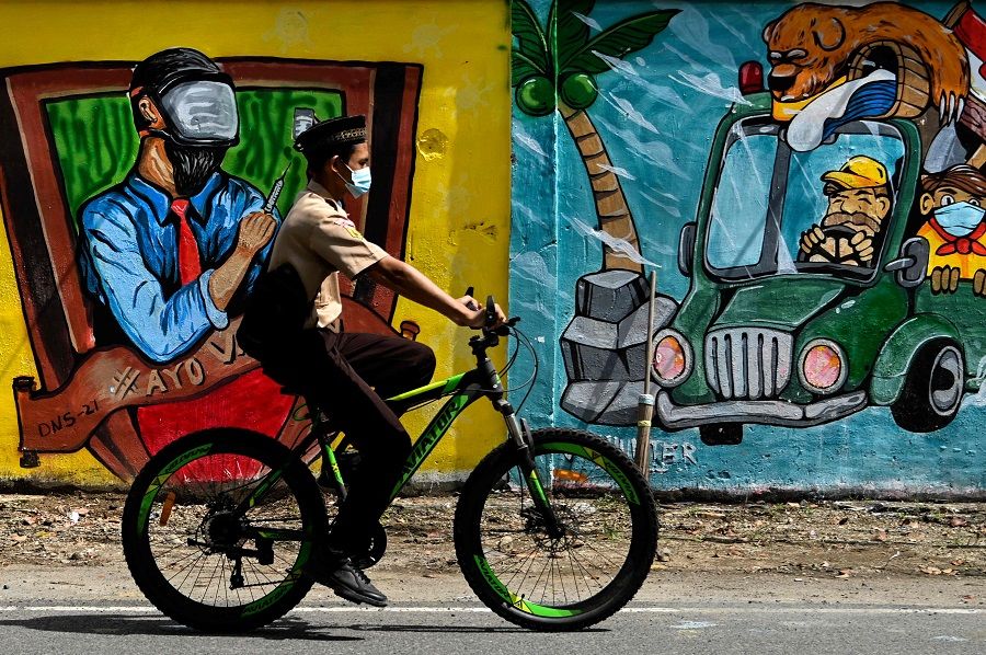 A student cycles past a wall mural in Banda Aceh, Indonesia, on 10 December 2021. (Chaideer Mahyuddin/AFP)