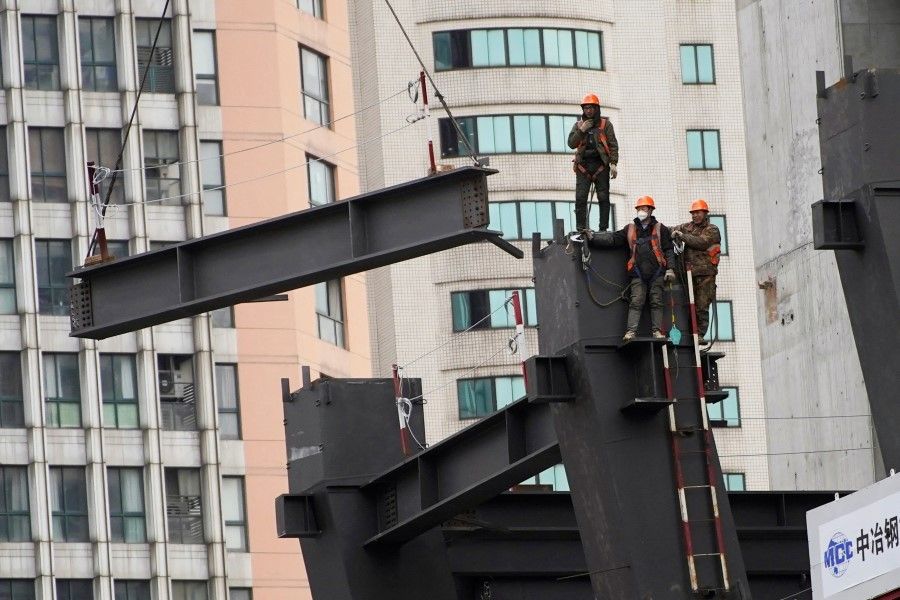Workers watch as a crane lifts a structure at a construction site in Shanghai, China, 14 January 2022. (Reuters/Aly Song)