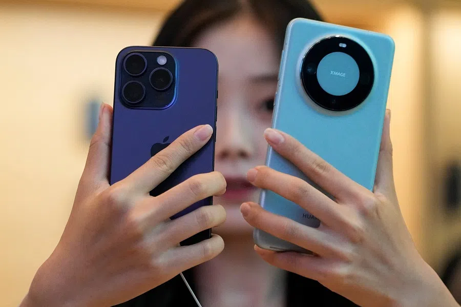 A woman looks at a new iPhone 15 Pro and a Huawei Mate 60 Pro as Apple's new iPhone 15 officially goes on sale across China, at an Apple store in Shanghai, China, on 22 September 2023. (Aly Song/Reuters)