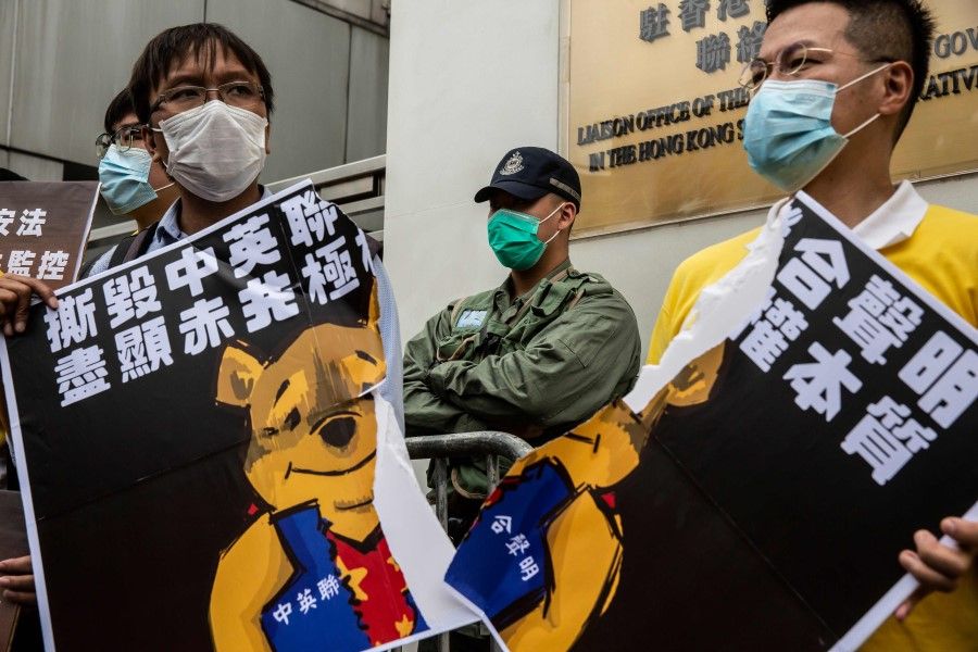 Pro-democracy activists tear a placard of Winnie-the-Pooh that represents Chinese President Xi Jinping during a protest against a proposed new security law outside the Chinese Liaison Office in Hong Kong, 24 May 2020. (Isaac Lawrence/AFP)