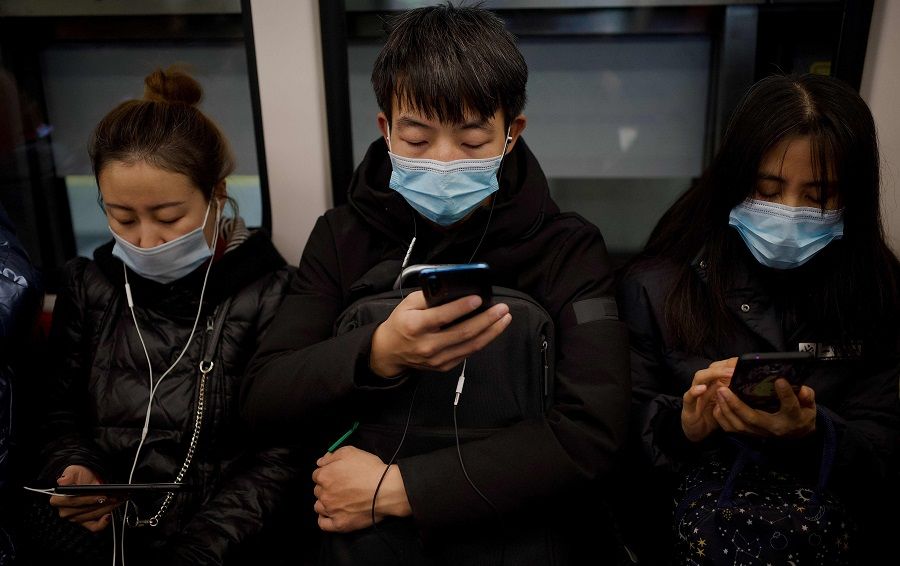 People wearing face masks use their mobile phone on a subway in Beijing on 19 December 2020. (Noel Celis/AFP)