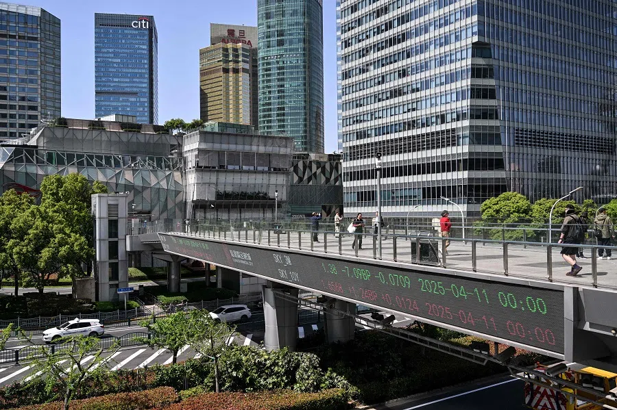 People walk across a footbridge showing a screen displaying financial market information at the financial district in Shanghai, China, on 14 April 2025. (Hector Retamal/AFP)