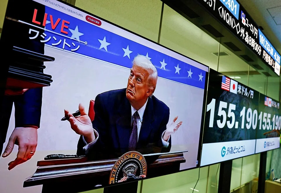 A screen broadcasting live footage shows US President Donald Trump gestures while signing executive orders next to screens displaying the current Japanese Yen exchange rate against the US dollar at a dealing room of the foreign exchange trading company Gaitame.com, in Tokyo, Japan, on 21 January 2025. (Issei Kato/Reuters)