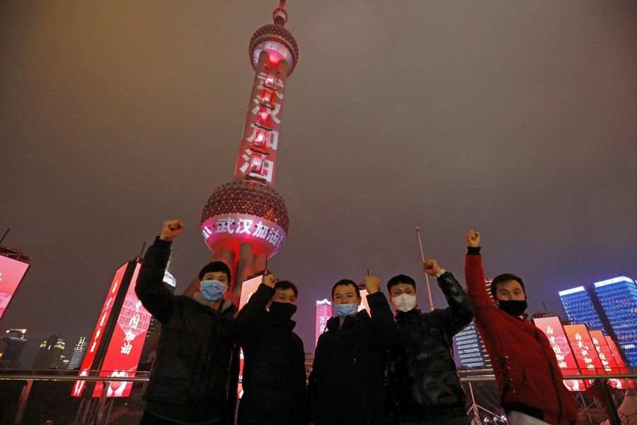 Tourists pose with the Oriental Pearl TV Tower in the background on 8 Feb 2020. Slogans with the words "武汉加油" (Wuhan, you can do it!) wrap the Shanghai landmark. (CNS)