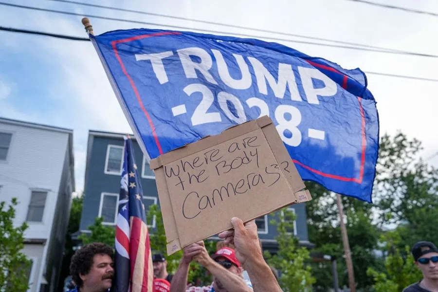 A placard is held in front of a Trump flag during a vigil for a man that was killed in a shooting involving US Immigration and Customs Enforcement, on 13 July 2026 in Biddeford, Maine.