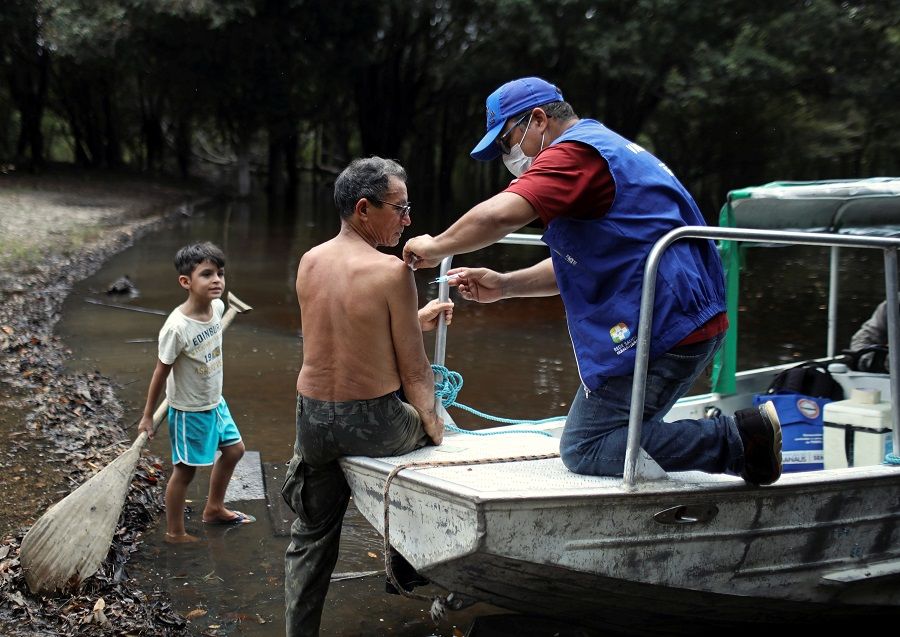 A health agent vaccinates an elderly man against flu and H1N1, as advised by health officials to facilitate diagnosis for coronavirus, amid the Covid-19 outbreak, along the Negro River banks, where the Ribeirinhos live, in Manaus, Brazil, on 2 April 2020. (Bruno Kelly/Reuters)