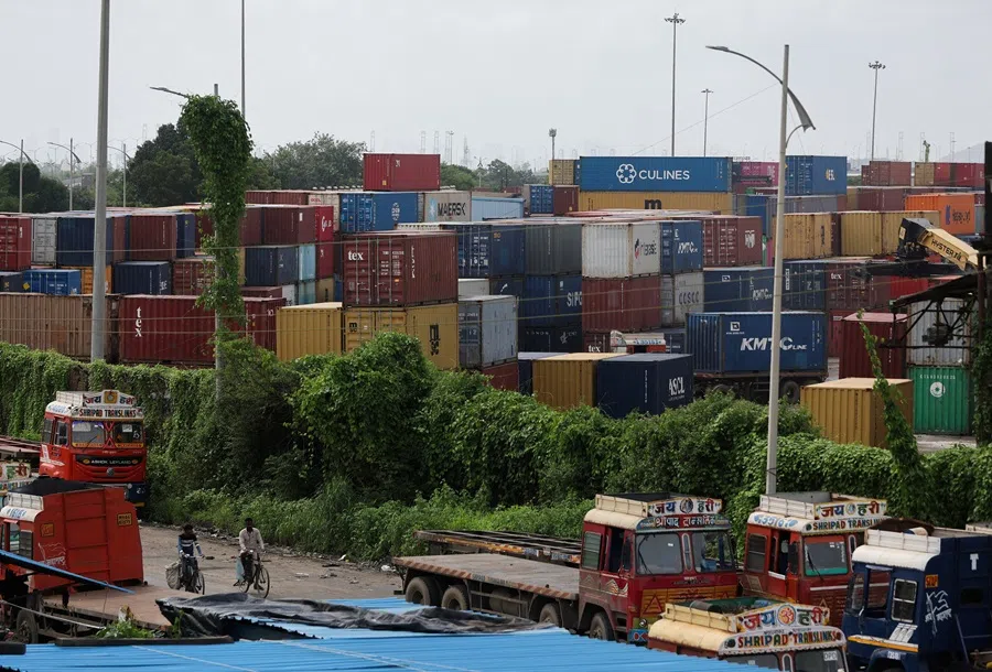 Men ride bicycles past shipping containers at a warehouse in Navi Mumbai, India, on 11 August 2025. (Francis Mascarenhas/Reuters)