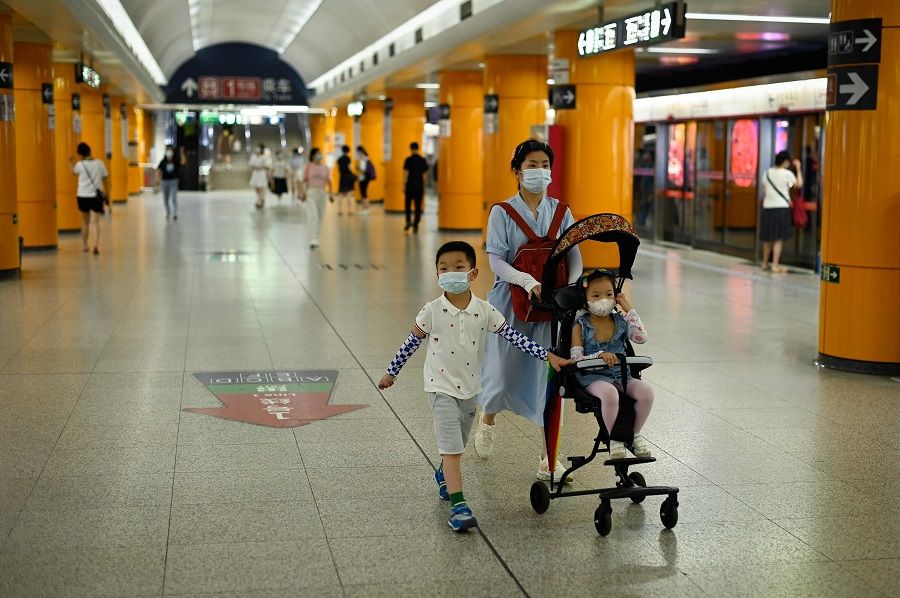 A woman walks in a subway station with two children in Beijing, China, on 5 July 2022. (Wang Zhao/AFP)