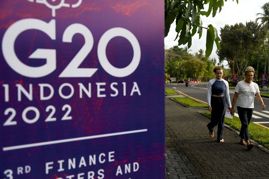 Foreign tourists walk past a banner of the G20 for the G20 Finance Ministers Meeting in Nusa Dua, on the Indonesia resort island of Bali on 14 July 2022. (Sonny Tumbelaka/Pool/AFP)
