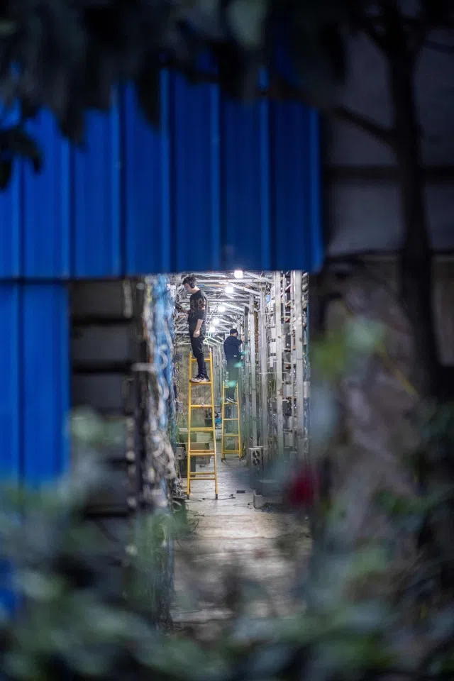 This photo taken on 31 March 2021 shows workers wearing noise-cancelling headphones as they adjust cryptocurrency mining rigs at a cryptocurrency farm in Dujiangyan in China's southwestern Sichuan province. (STR/AFP)