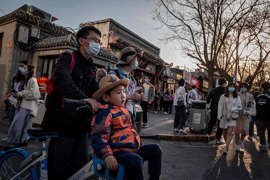 A young boy (centre) is pushed along on a bicycle on a street in Beijing, China, on 4 April 2021. (Nicolas Asfouri/AFP)