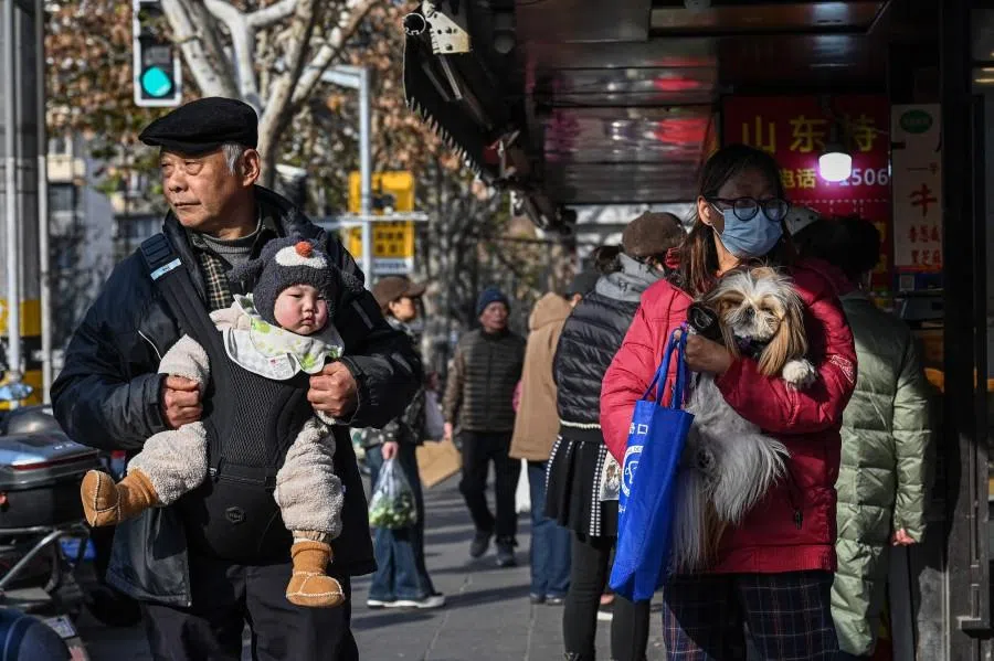 An elderly man carries a baby alongside a woman holding a dog on a street in Shanghai on 9 January 2026.