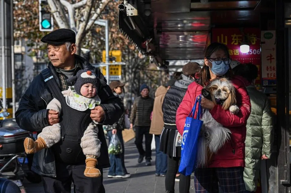 An elderly man carries a baby alongside a woman holding a dog on a street in Shanghai on 9 January 2026. (Jade Gao/AFP)