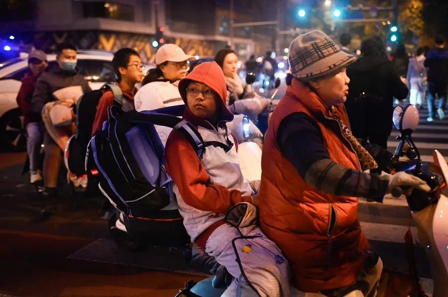 People riding electric bicycles cross a street in Beijing on 17 October 2024. (Wang Zhao/AFP)