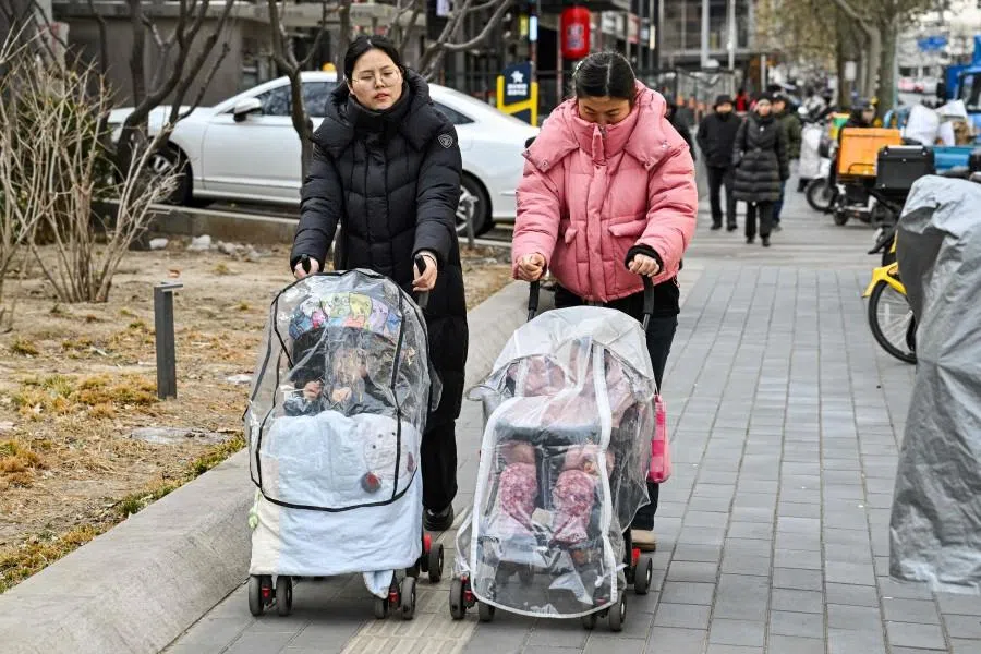 Women push baby strollers as they walk along a street in Beijing on 4 January 2026. (Adek Berry/AFP)