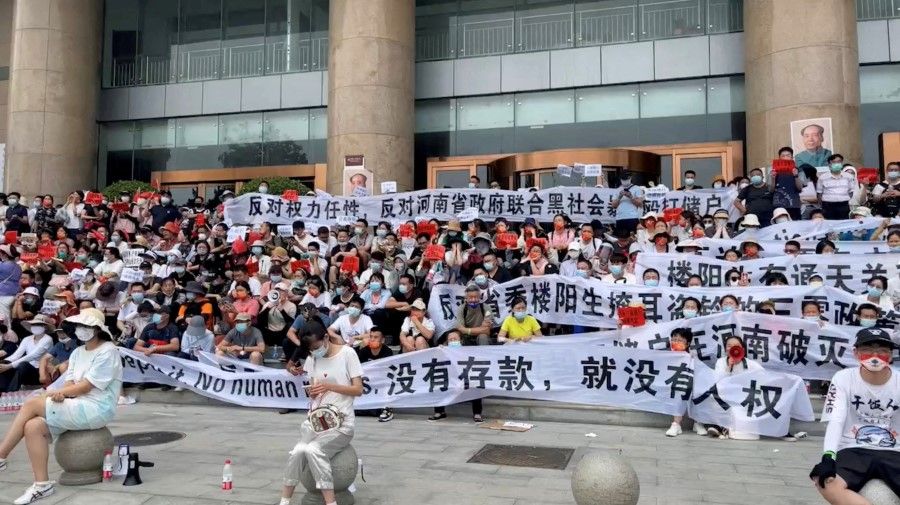 Demonstrators hold banners during a protest over the freezing of deposits by rural-based banks, outside a People's Bank of China building in Zhengzhou, Henan province, China, 10 July 2022, in this screengrab taken from video obtained by Reuters. (Handout via Reuters)