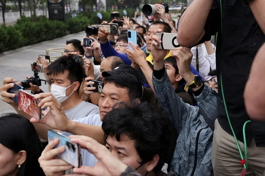 People take photos from a side street as a motorcade believed to be carrying US President Donald Trump drives past during his visit to China in Beijing, China, on 15 May 2026.