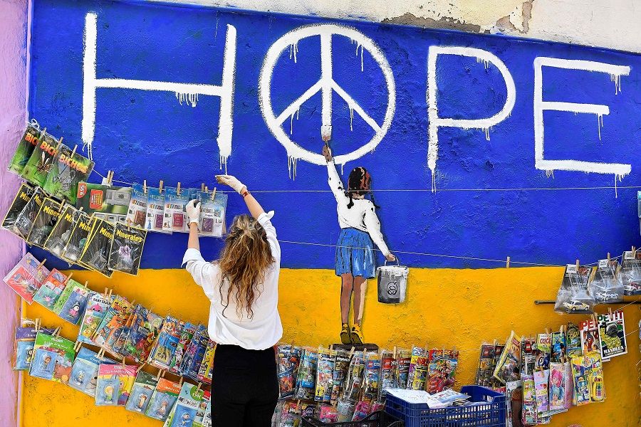 A newsagent picks up magazines next to a mural by Italian urban artist Salvatore Benintende aka "TV BOY" depicting a girl painting a peace symbol on an Ukraine's flag, reading "Hope" in Barcelona, Spain, on 30 April 2022. (Pau Barrena/AFP)