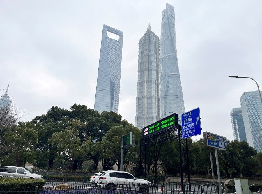 Cars travel past a display showing Shanghai and Shenzhen stock indexes near the Shanghai Tower and other skyscrapers at the Lujiazui financial district in Shanghai, China, on 5 February 2024. (Xihao Jiang/Reuters)