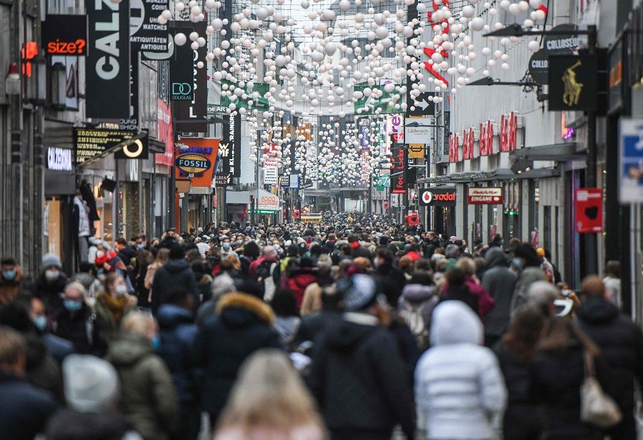 People are seen wearing face masks as they walk in a pedestrian street among shops and Christmas decorations in the city of Cologne, Germany, on 18 December 2021. (Ina Fassbender/AFP)
