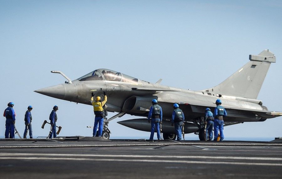 This file photo taken on 5 June 2021 shows crew members standing next to a Rafale jet fighter on the deck of the French aircraft carrier Charles-de-Gaulle, off the coast of Toulon. (Nicolas Tucat/AFP)