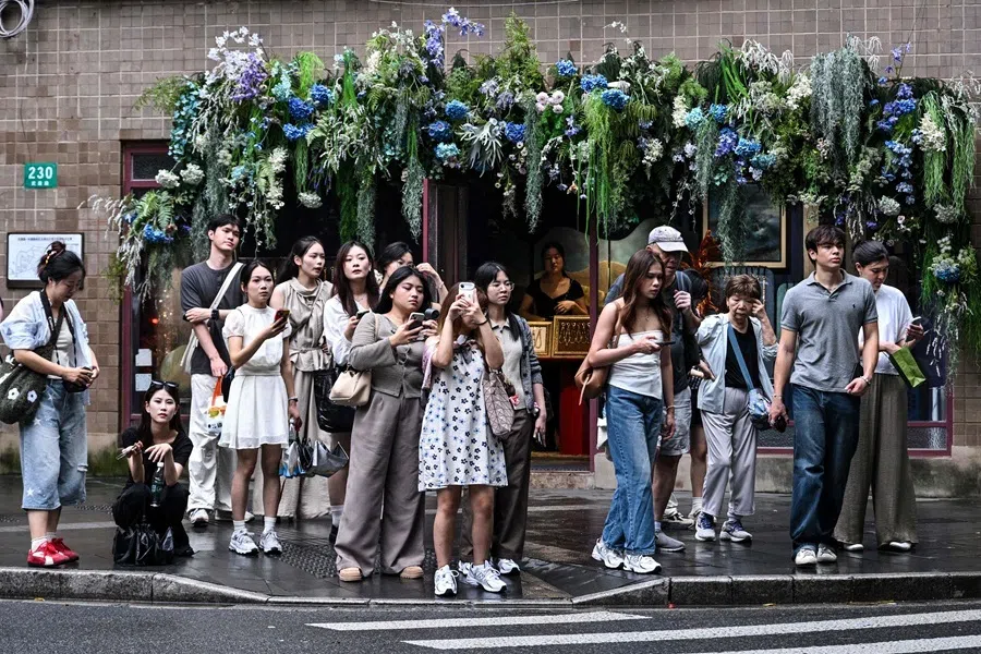 People wait to cross a street in the Xuhui district in Shanghai on 14 August 2026.