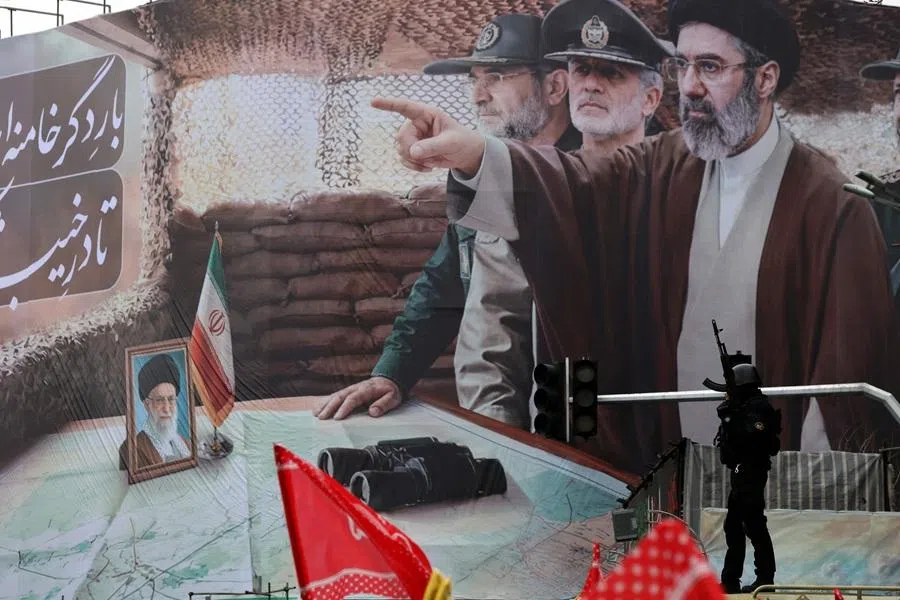 A member of the Iranian security forces stands guard next to a huge billboard of Iran's newly nominated supreme leader Ayatollah Mojtaba Khamenei (pointing) in Tehran on 13 March 2026. (AFP)