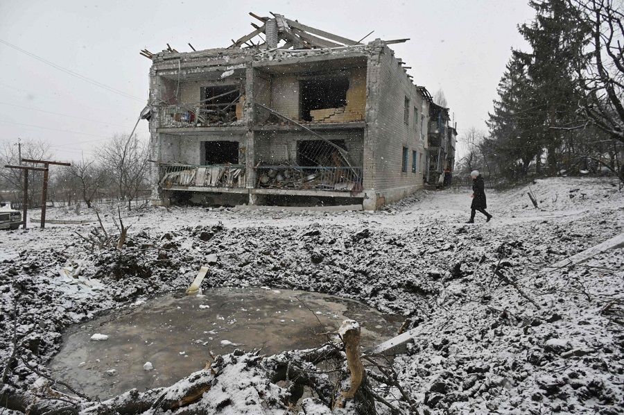A local resident walks past a crater and a damaged residential building following a recent aerial bombardment in Kupiansk, Kharkiv region, on 18 February 2024, amid the Russian invasion of Ukraine. (Sergey Bobok/AFP)