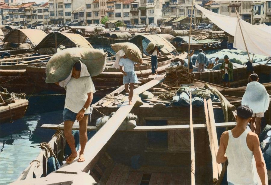 A busy scene of people at work in Boat Quay in the 1950s. Smaller goods vessels were dependent on manual labour to shift goods.