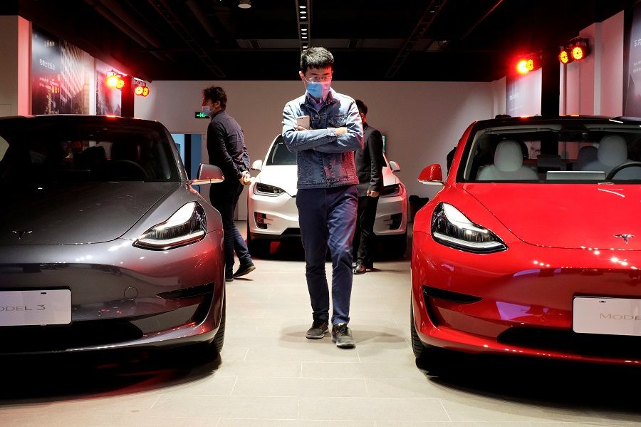A man wearing a face mask walks by Tesla Model 3 sedans and Tesla Model X sport utility vehicle at a new Tesla showroom in Shanghai, China, 8 May 2020. (Yilei Sun/File Photo/Reuters)