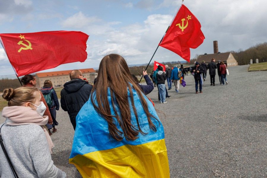 People with Soviet and Ukrainian flags arrive for a commemoration ceremony to mark the 77th anniversary of the liberation of the Buchenwald Nazi concentration camp at the camp's memorial site in Buchenwald, near Weimar, eastern Germany, on 10 April 2022. (Jens Schlueter/AFP)