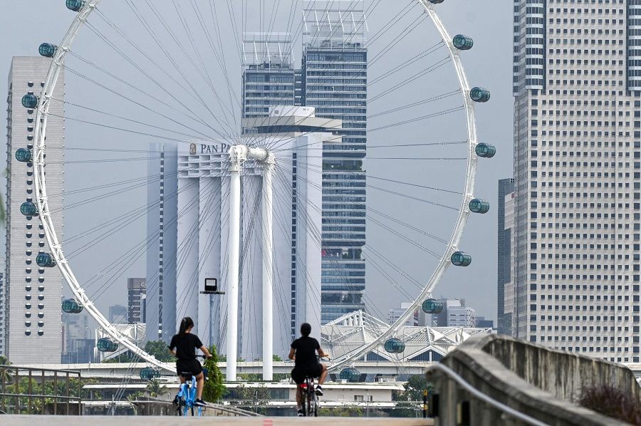 People ride bicycles near the Singapore Flyer in Singapore on 22 July 2022. (Roslan Rahman/AFP)