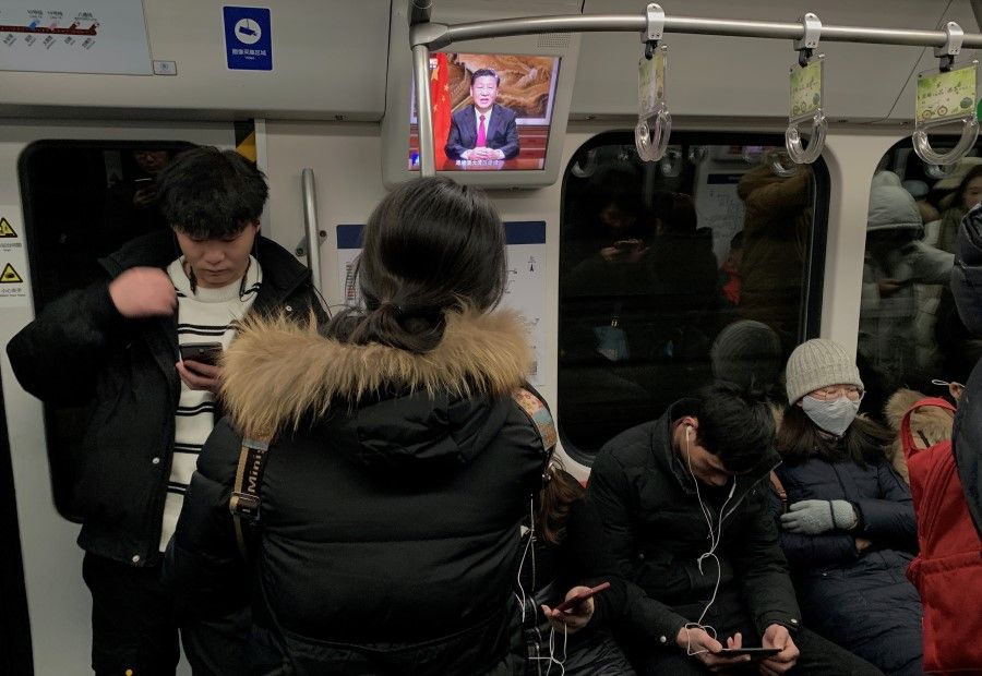 Passengers are seen next to a screen broadcasting news of Chinese President Xi Jinping addressing a New Year's Eve speech, on a subway train in Beijing, 31 December 2019. (Tingshu Wang/REUTERS)