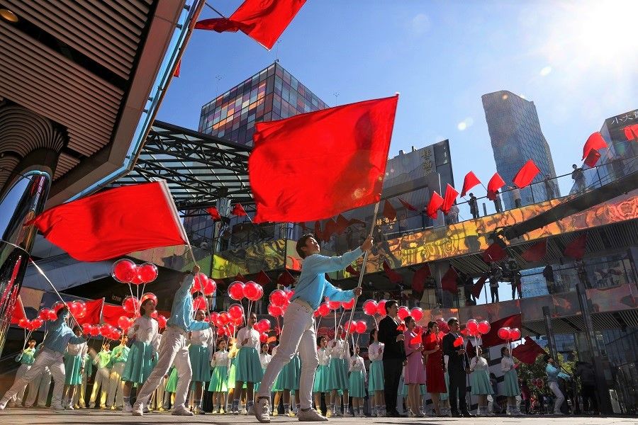 People wave red flags during the filming of a Communist Party of China propaganda video in an upscale shopping district in the Sanlitun area in Beijing, China, 19 October 2021. (Thomas Peter/Reuters)
