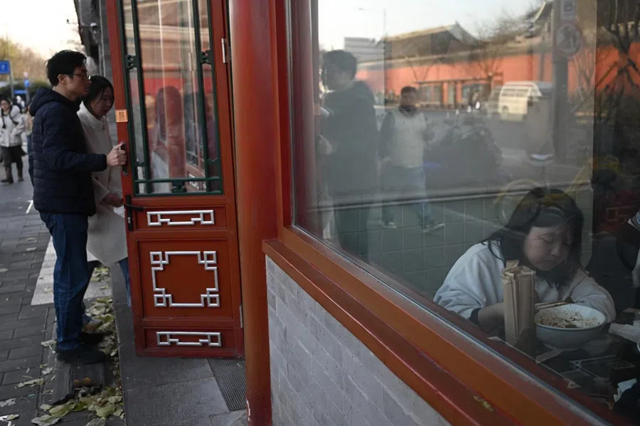 A couple enters a restaurant as a girl eats in an area popular with tourists in Beijing, China, on 30 November 2025. (Pedro Pardo/AFP)