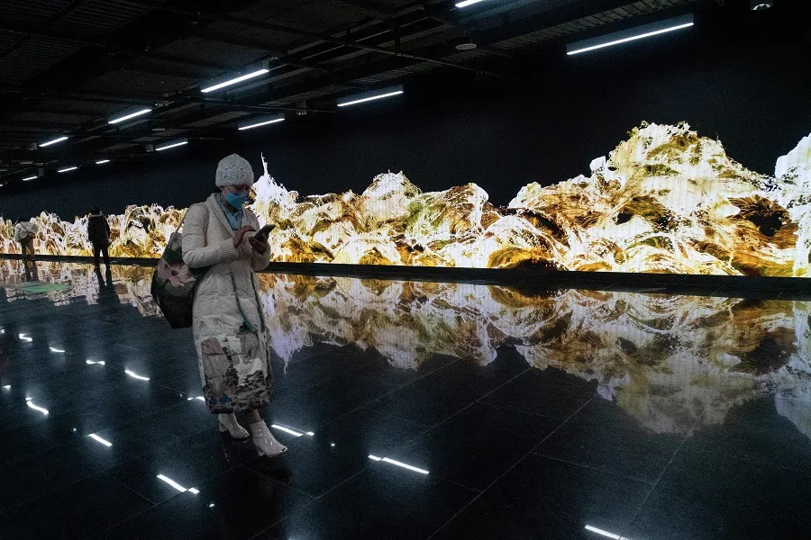 A woman walks past a 112-metre-long installation entitled "Gold Waves" by teamLab at Shanghai's Lujiazui subway station in China on 26 January 2022. (AFP)