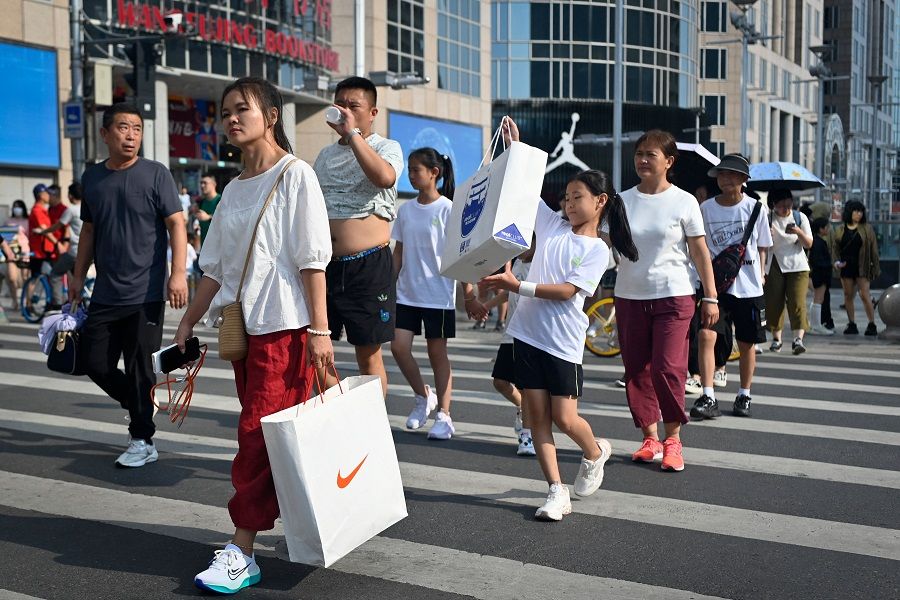 Pedestrians cross a street in a business district in Beijing on 14 August 2023. (Wang Zhao/AFP)