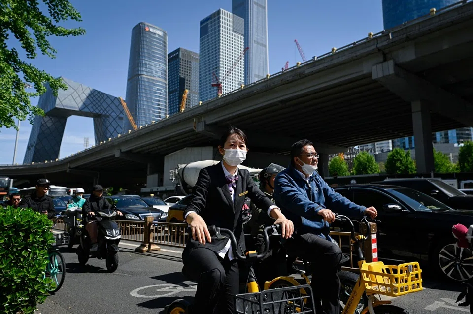 People ride bicycles along a street at a business district in Beijing, China, on 16 April 2024. (Wang Zhao/AFP)