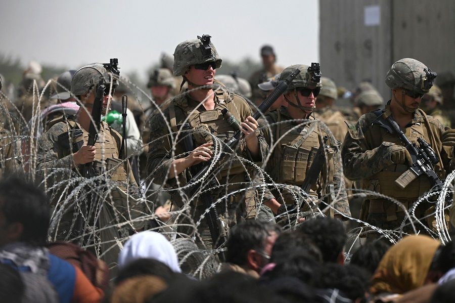 US soldiers stand guard behind barbed wire as Afghans sit on a roadside near the military part of the airport in Kabul, Afghanistan, on 20 August 2021, hoping to flee from the country after the Taliban's military takeover of Afghanistan. (Wakil Kohsar/AFP)