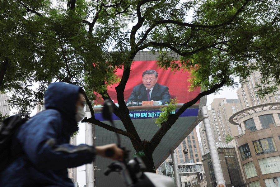A man wearing a face mask rides past a giant screen showing Chinese President Xi Jinping in Beijing, China, 10 May 2022. (Tingshu Wang/Reuters)