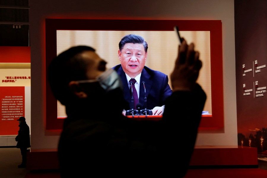 A visitor holds his mobile phone near a screen showing Chinese President Xi Jinping at Wuhan Parlor Convention Center in Wuhan, Hubei province, China, 31 December 2020. (Tingshu Wang/Reuters)