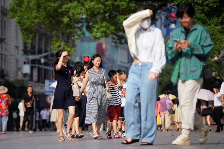 People walk on a street as they shield themselves from the sun, amid a heatwave alert in Shanghai, China, 11 July 2023. (Aly Song/Reuters)
